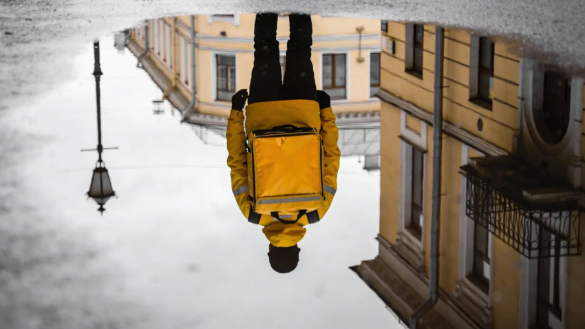 Велокурьер быстро едет по городской улице с термокоробом за спиной Велокурьер быстро едет по городской улице с термокоробом за спиной